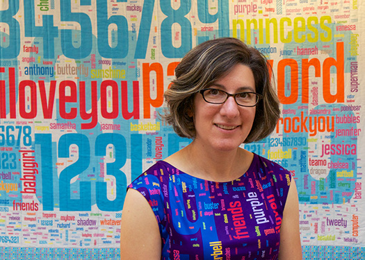 author wearing a multicolored dress with common passwords on it, in front of a large quilt with the same theme