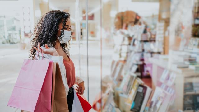 Woman in medical mask holds shopping bags in front of shop window