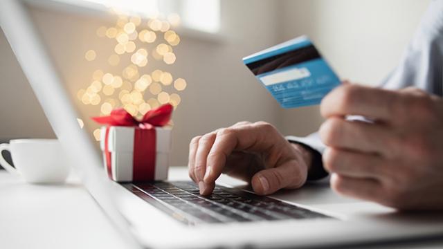 person holding credit card while using a laptop with holiday decorations in the background