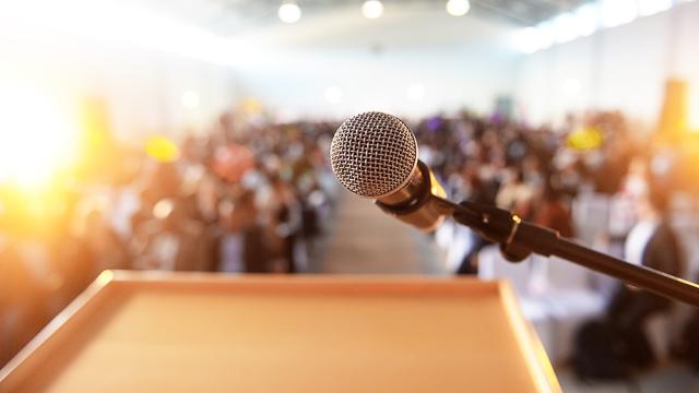 microphone on a podium in front of crowd of people at a meeting